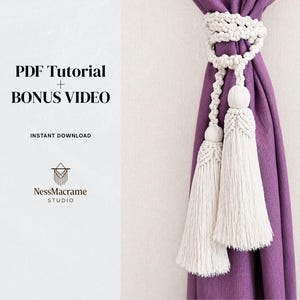 Pode incluir: Amarrador de cortina de macramé branco com duas borlas, exibido em uma cortina roxa. A imagem inclui o texto "PDF Tutorial + Bonus Video" e "Instant Download". O logotipo NessMacrame Studio também é visível.