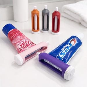 Puede incluir: Varios tubos de pasta de dientes y exprimidores de tubos en diferentes colores. Los tubos son rosas y azules, con texto blanco. Los exprimidores son rosas, morados, naranjas, grises y rojos. Fondo blanco.