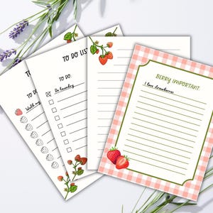 Könnte beinhalten: Ein Stapel weißer Notizblöcke mit Erdbeerillustrationen und dem Text "TO DO LIST" und "BERRY IMPORTANT". Ein Notizblock hat einen rosa Vichy-Rand. Lavendelzweige sind im Hintergrund.