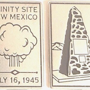 May include: Two rectangular metal pins. One pin features the text "TRINITY SITE NEW MEXICO" above a stylized atomic cloud and the date "JULY 16, 1945". The other pin depicts a monument with a mountain backdrop.