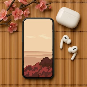Könnte beinhalten: Ein schwarzes Smartphone mit einem Landschaftsbild eines Waldes und Hügeln auf dem Bildschirm. Das Telefon liegt auf einer Bambusmatte mit einem Paar weißen kabellosen Ohrhörern und einem weißen Ladeetui.