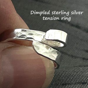 May include: A dimpled sterling silver tension ring. The ring has a hammered texture and a unique, open design. The text "Dimpled sterling silver tension ring" is visible in the image.
