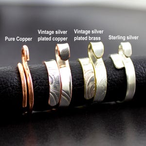 May include: A close-up of four adjustable rings. The rings are labeled: "Pure Copper", "Vintage silver plated copper", "Vintage silver plated brass", and "Sterling silver". The rings are displayed on a black surface.