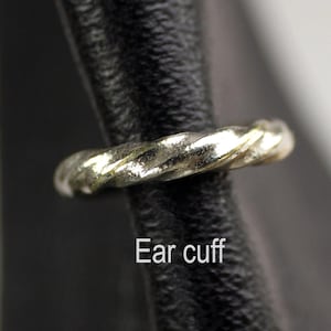 May include: A silver-colored ear cuff with a twisted rope design. The jewelry is shown on a black background. The text "Ear cuff" is displayed below the ear cuff.