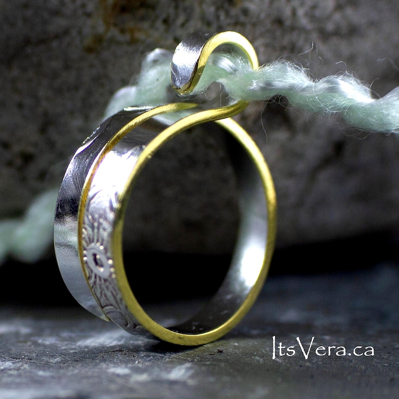 Może przedstawiać: Zbliżenie srebrnego pierścionka ze złotą obrączką. Srebrna obrączka ma kwiatowy wz&oacute;r. Pierścionek zawieszony jest na jasnozielonej nici. Adres strony internetowej itsVera.ca jest widoczny w prawym dolnym rogu.