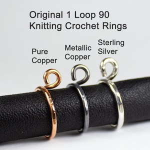 May include: Three metal knitting crochet rings, one in pure copper, one in metallic copper, and one in sterling silver. The rings are all 90 degree loops and are displayed on a black surface.