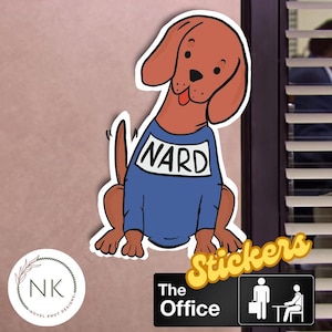 May include: A cartoon sticker of a brown dog wearing a blue shirt with the word "NARD" on it. The sticker is on a pink wall with a black and white "The Office" logo below it.