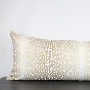 May include: A long, rectangular lumbar pillow with a beige background and a white spotted pattern resembling a fawn's coat.