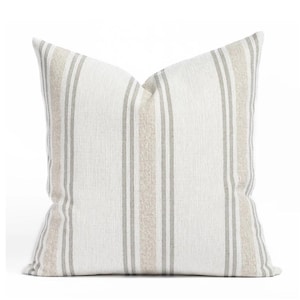 May include: A square decorative pillow with a striped pattern. The pillow features vertical stripes in shades of white, gray, and beige. The pillow is made of a textured fabric and is designed for home decor.