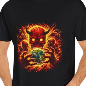May include: Black t-shirt featuring a fiery graphic of a horned skull with glowing eyes, surrounded by flames and smaller skulls. The skull appears to be holding a globe. A bold, eye-catching design.