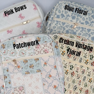 May include: Four quilted cosmetic bags with different patterns. One is white with pink bows and the text "Pink Bows". Another is blue with a floral pattern and the text "Blue Floral". The third is patchwork with the text "Patchwork". The last is cream with the text "Cream Vintage Floral".