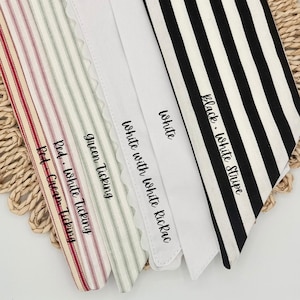 May include: A collection of five fabric strips featuring various patterns and colors: red and cream ticking, red and white ticking, green ticking, white with white rickrack trim, and black and white stripes, each labeled with its respective name.