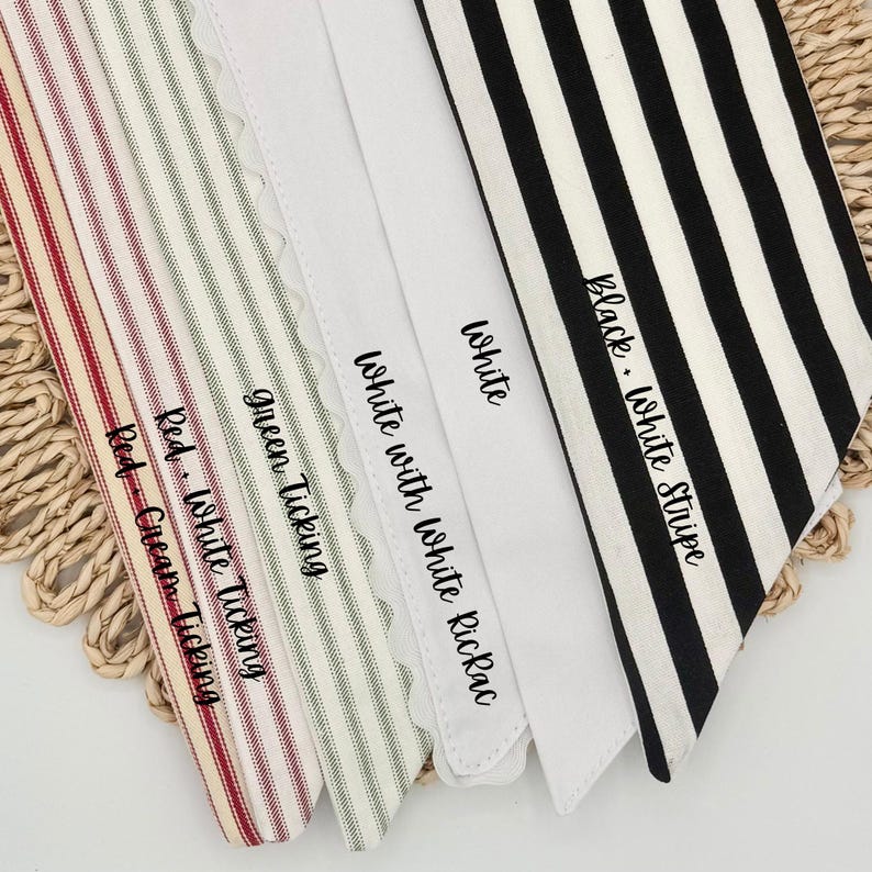 May include: A collection of five fabric strips featuring various patterns and colors: red and cream ticking, red and white ticking, green ticking, white with white rickrack trim, and black and white stripes, each labeled with its respective name.