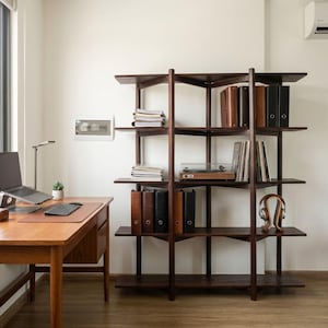 May include: A dark wood open shelving unit with five tiers, holding stacks of papers, several vertical binders, a wooden record player, and a pair of headphones. The unit stands next to a wooden desk with a laptop, keyboard, and a small potted plant.