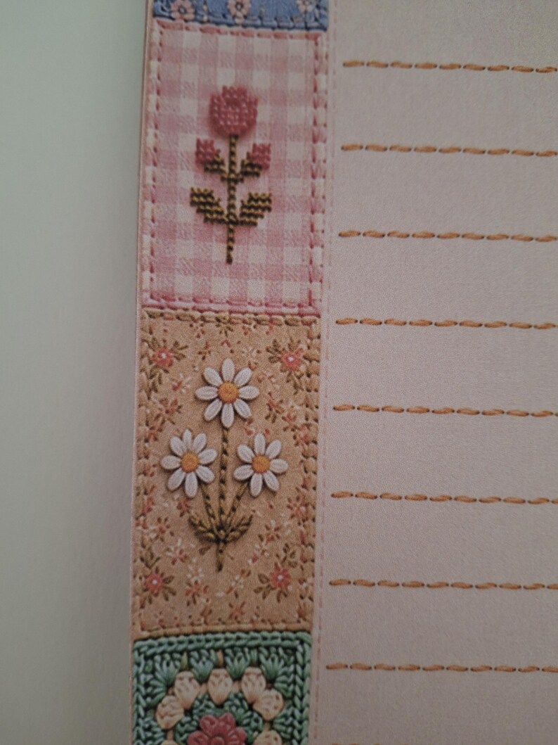 May include: A sheet of stationery featuring a vertical border of patchwork-style squares with floral and crochet patterns in pink, beige, and green. The right side of the paper is light pink with horizontal lines marked by orange dashed stitches.