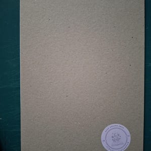 Puede incluir: Una pieza rectangular de cart&oacute;n texturizado de color marr&oacute;n claro con un acabado mate. En la esquina inferior derecha, hay una peque&ntilde;a pegatina blanca circular con un dibujo lineal de flores en un libro y el texto Etsy Online Shop Scrapbookingdream.