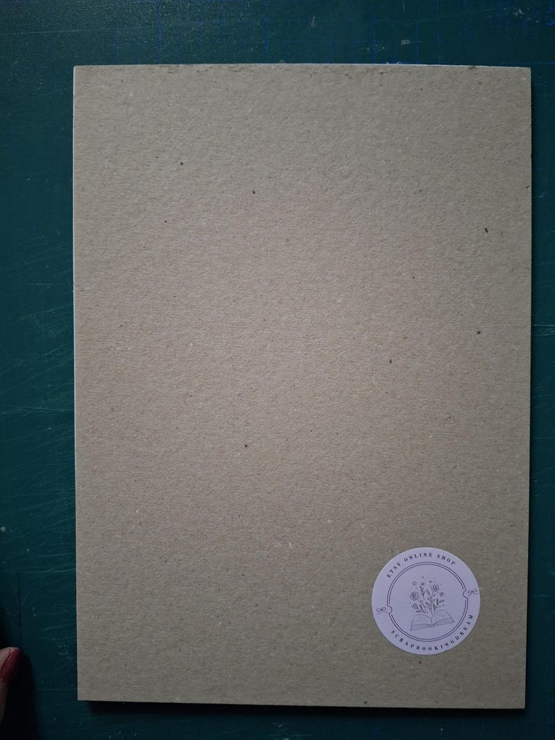 Puede incluir: Una pieza rectangular de cart&oacute;n texturizado de color marr&oacute;n claro con un acabado mate. En la esquina inferior derecha, hay una peque&ntilde;a pegatina blanca circular con un dibujo lineal de flores en un libro y el texto Etsy Online Shop Scrapbookingdream.