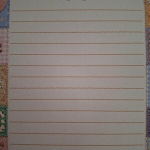 Puede incluir: Una hoja de papel de carta rectangular con un centro blanco y l&iacute;neas horizontales naranjas. La parte superior est&aacute; decorada con un lazo y motivos florales en punto de cruz rosa. El borde es un mosaico de peque&ntilde;os cuadrados coloridos.
