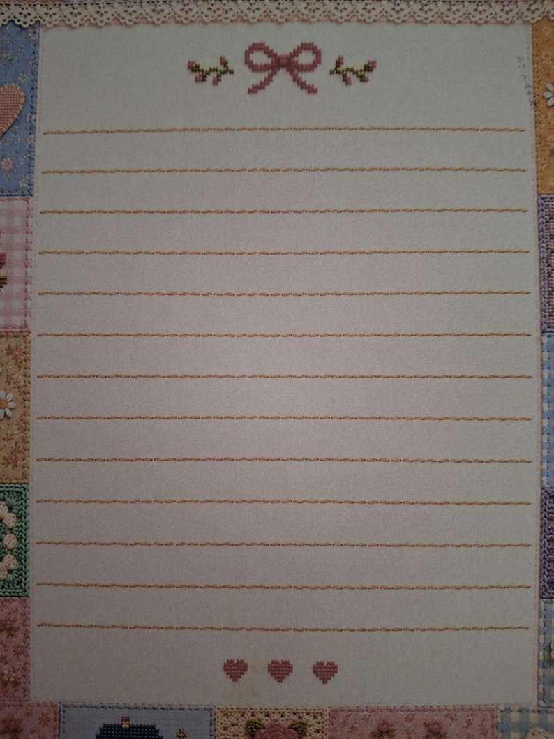 Puede incluir: Una hoja de papel de carta rectangular con un centro blanco y l&iacute;neas horizontales naranjas. La parte superior est&aacute; decorada con un lazo y motivos florales en punto de cruz rosa. El borde es un mosaico de peque&ntilde;os cuadrados coloridos.