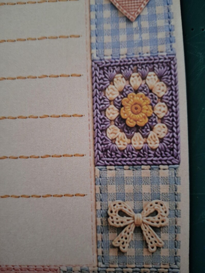 Puede incluir: Una hoja de papel de carta con una zona de escritura beige claro y l&iacute;neas horizontales cosidas en hilo dorado. El borde derecho muestra una franja vertical de tela de cuadros vichy azul y blanca, un cuadrado de ganchillo morado con una flor amarilla y un lazo crema.