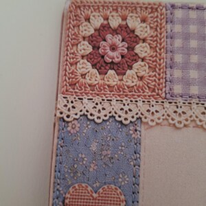 May include: A rectangular card featuring a patchwork design with a square crochet motif in shades of pink and cream, a purple gingham square, and a blue floral panel. A cream-coloured lace trim separates the sections, and a pink heart is attached.