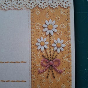 Puede incluir: Una hoja de papel de carta decorativa con un borde vertical sobre un fondo amarillo mostaza estampado con peque&ntilde;as flores blancas. El borde muestra un ramo de tres margaritas blancas con centros amarillos atadas con un lazo rosa.