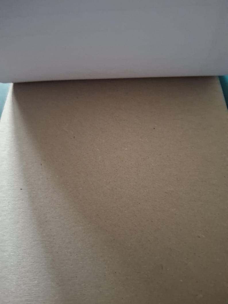 Puede incluir: Un bloc rectangular de papel kraft de color marr&oacute;n claro con una textura lisa y mate. El borde superior muestra una gruesa tira de encuadernaci&oacute;n blanca, mientras que el resto de la superficie presenta un color beige neutro y uniforme.