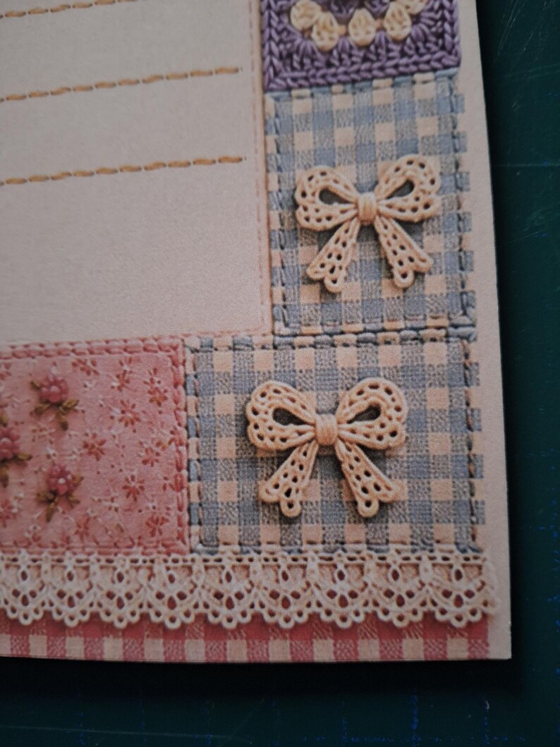 Puede incluir: Una hoja de papel de carta con un dise&ntilde;o de patchwork que incluye cuadros vichy azul claro, una secci&oacute;n de flores rosas y un borde de encaje color crema. Dos lazos decorativos color crema est&aacute;n fijados sobre los cuadros y el papel tiene l&iacute;neas.
