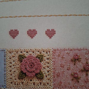Puede incluir: Una pieza textil con puntadas horizontales de color canela sobre tres peque&ntilde;os corazones rosas bordados en punto de cruz. Debajo, un motivo cuadrado de ganchillo con una rosa rosa y hojas verdes junto a una tela floral rosa con encaje.