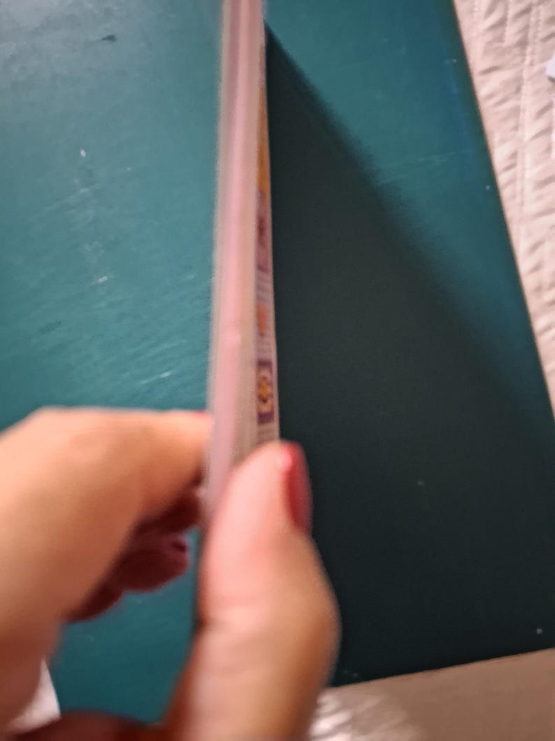 Puede incluir: Un folleto rectangular delgado con una cubierta de color verde azulado oscuro y un lomo claro. El perfil lateral revela varias p&aacute;ginas internas con peque&ntilde;as ilustraciones cuadradas de colores visibles en el borde del papel.