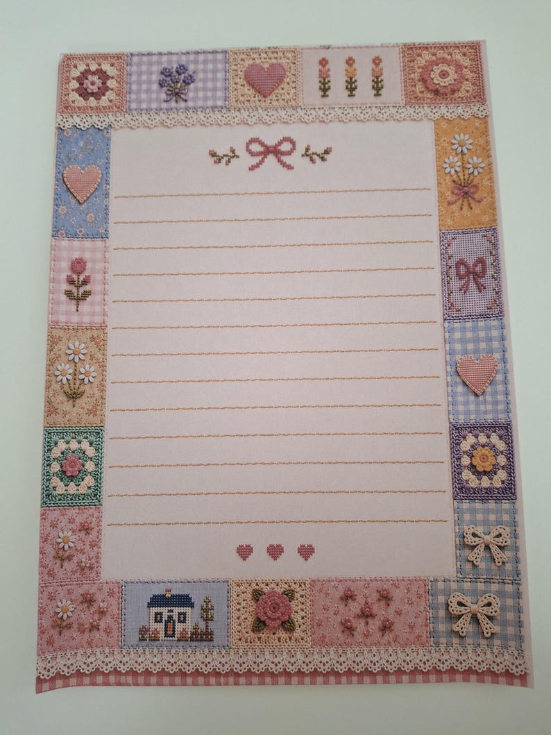 May include: A rectangular sheet of stationery featuring a light pink centre with horizontal lines and a decorative border composed of various square patches. The border includes embroidered motifs of flowers, hearts, bows, and a small house.