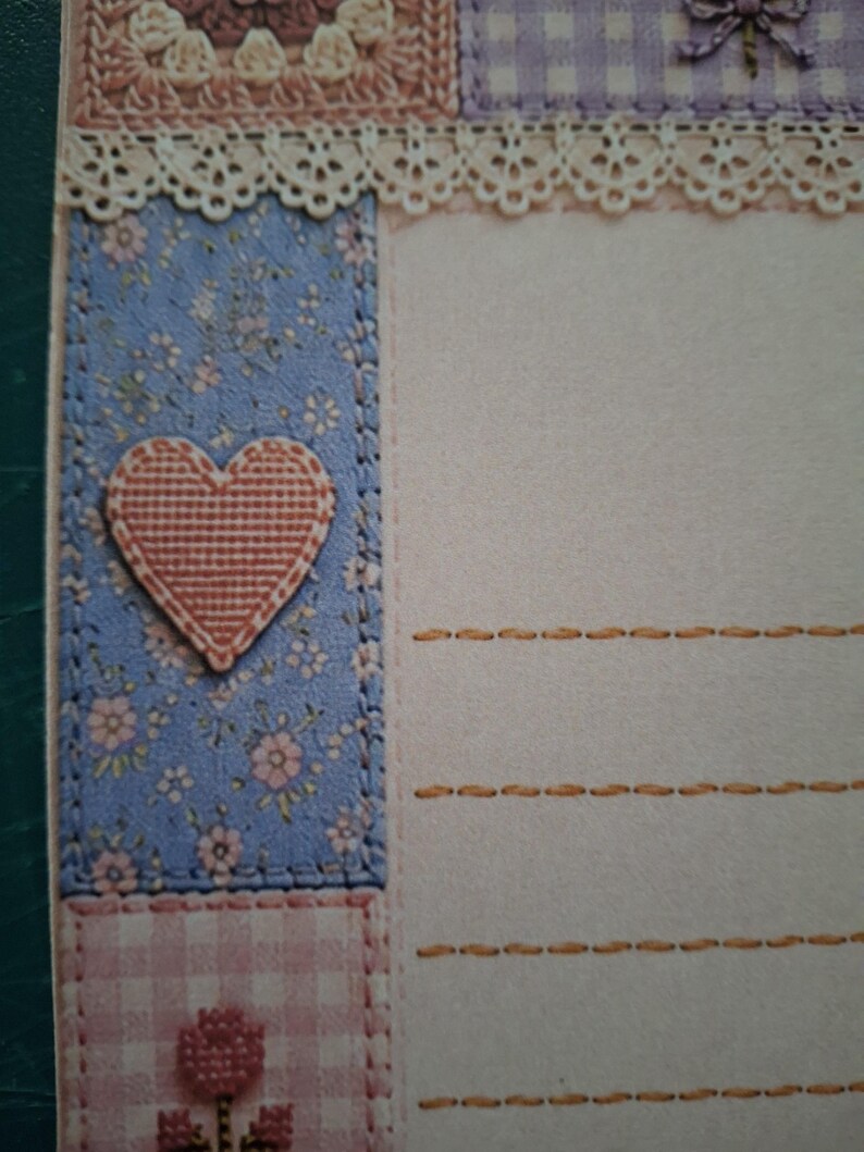 Puede incluir: Una hoja de papel de carta con una zona de escritura color crema y l&iacute;neas horizontales naranjas discontinuas. El borde izquierdo muestra un patr&oacute;n floral azul con un coraz&oacute;n texturizado, mientras que la parte superior est&aacute; adornada con encaje y un cuadro vichy morado.