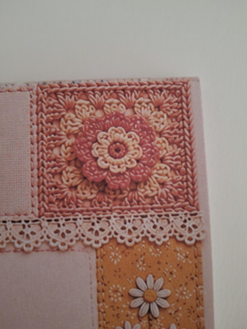 May include: A square crochet motif featuring a central pink and cream flower pattern, bordered by a delicate white lace trim. Below the lace, a mustard yellow panel displays a repeating white daisy print with additional white daisy embellishments.