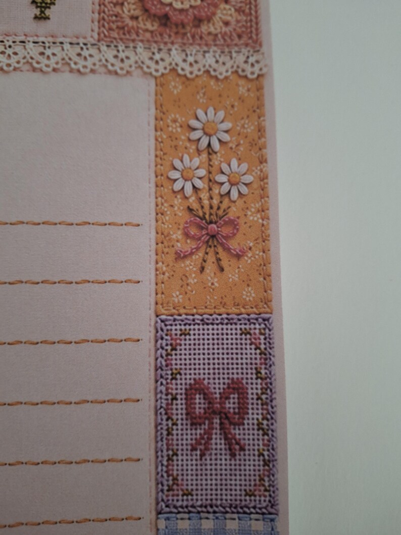 May include: A light pink stationery sheet featuring horizontal stitched lines, a white lace trim, and a vertical panel decorated with a bouquet of three white daisies tied with a pink bow, followed by a lavender cross-stitch square with a pink bow.