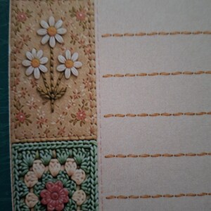 Puede incluir: Una hoja de papel de carta con un borde decorativo vertical en el lado izquierdo. El borde incluye una secci&oacute;n de cuadros rosas, un panel floral beige con tres margaritas blancas y un motivo de ganchillo cuadrado de color verde.