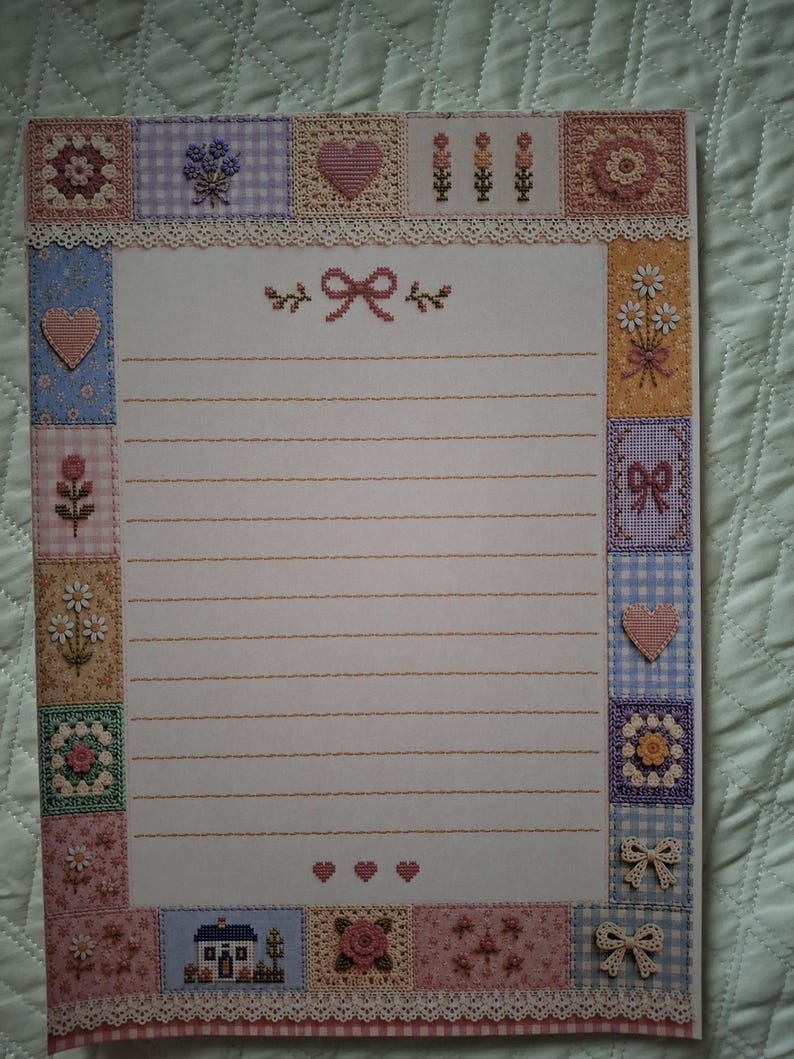 Puede incluir: Una hoja de papel de carta rectangular con un borde decorativo compuesto por varios cuadrados con patrones de punto de cruz, incluyendo flores, corazones, lazos y una casa. El centro tiene l&iacute;neas horizontales y un peque&ntilde;o icono de lazo.