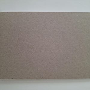 以下が含まれることがあります： 平らでマットな表面と目に見える繊維状の質感を持つ、明るい茶色の長方形の厚紙。素材は均一な色で、清潔でまっすぐなエッジのデザインが特徴であり、シンプルでニュートラル、かつ機能的な外観を呈しています。