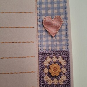 May include: A light pink stationery sheet with horizontal orange stitched lines on the left side. The right border features a vertical strip of blue and white gingham fabric, a pink heart applique, and a square purple crochet flower motif.