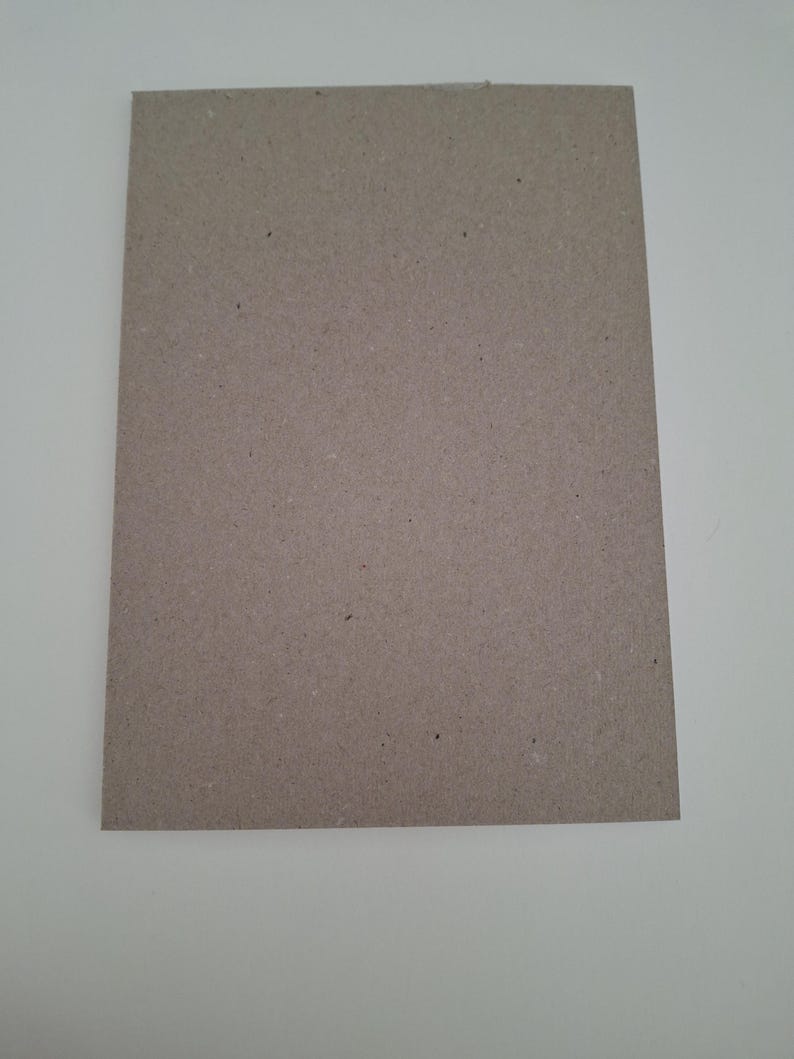 Puede incluir: Una hoja rectangular de cart&oacute;n de color marr&oacute;n claro con textura y un acabado mate plano. La superficie muestra sutiles variaciones de color y peque&ntilde;as motas oscuras, caracter&iacute;sticas del material de papel reciclado con bordes rectos.