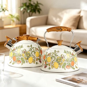 May include: Two cream-coloured tea kettles with a lemon and foliage pattern. Each kettle features a wood-grain handle and lid knob, a stainless steel spout with a wood-grain lever, and the name Molly printed on the handle of the right kettle.