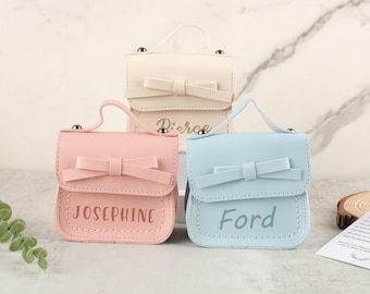 May include: Three small, pastel-colored purses with bow accents and top handles. The purses are in pink, light blue, and off-white. Each purse has a name printed on the front: "Josephine", "Ford", and "Pierce".