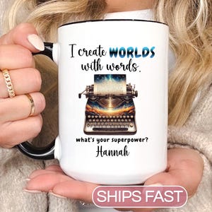 May include: White ceramic mug with a black handle and rim. The mug features the text "I create WORLDS with words" and a vintage typewriter illustration. Below the typewriter is the text "what's your superpower? Hannah."