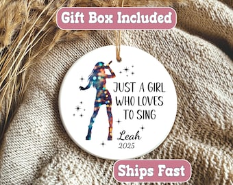 May include: A white ceramic ornament with a silhouette of a singer holding a microphone, with a colorful pattern. Text reads "JUST A GIRL WHO LOVES TO SING" and a name and year. Includes a gold string for hanging.