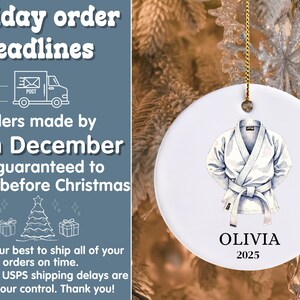 May include: White ceramic Christmas ornament featuring a watercolor illustration of a karate gi. The ornament includes the name "OLIVIA" and the year "2025". The ornament hangs from a gold string.