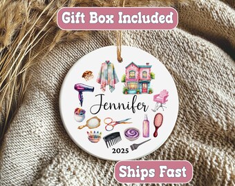 May include: A white ceramic ornament featuring a salon theme. It includes a pink salon chair, a hair dryer, scissors, and a building illustration. The name "Jennifer" and the year "2025" are also displayed.
