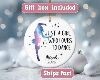 May include: A round white ceramic ornament featuring a galaxy-patterned silhouette of a dancer, black text reading "JUST A GIRL WHO LOVES TO DANCE", the name "Nicole", and the year "2026", accented with small black star icons.