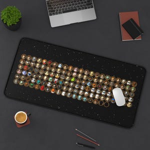 Puede incluir: Una alfombrilla de escritorio rectangular negra con un fondo de temática espacial y una cuadrícula densa de iconos circulares. Cada icono contiene una pequeña cabeza de personaje estilizada que parece una figura de juguete. Un ratón blanco descansa sobre ella.