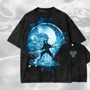 以下が含まれることがあります： 2つの黒いTシャツ。大きなシャツは、青いエネルギー効果のある円の中に杖を持った人物の青いグラフィックが特徴です。小さなシャツは前面に青いシンボルが付いています。どちらのシャツも色あせたヴィンテージルックです。