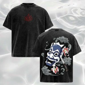 以下が含まれることがあります： 前面に赤い炎のデザイン、背面に青と白のマスクグラフィックが施された黒いTシャツ。 ヴィンテージ感のあるウォッシュ加工が施され、クルーネックです。