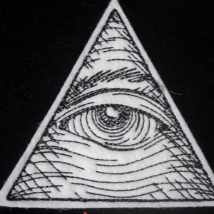 May include: A black and white embroidered patch depicting an eye within a triangle. The eye is detailed with a pupil and an iris.